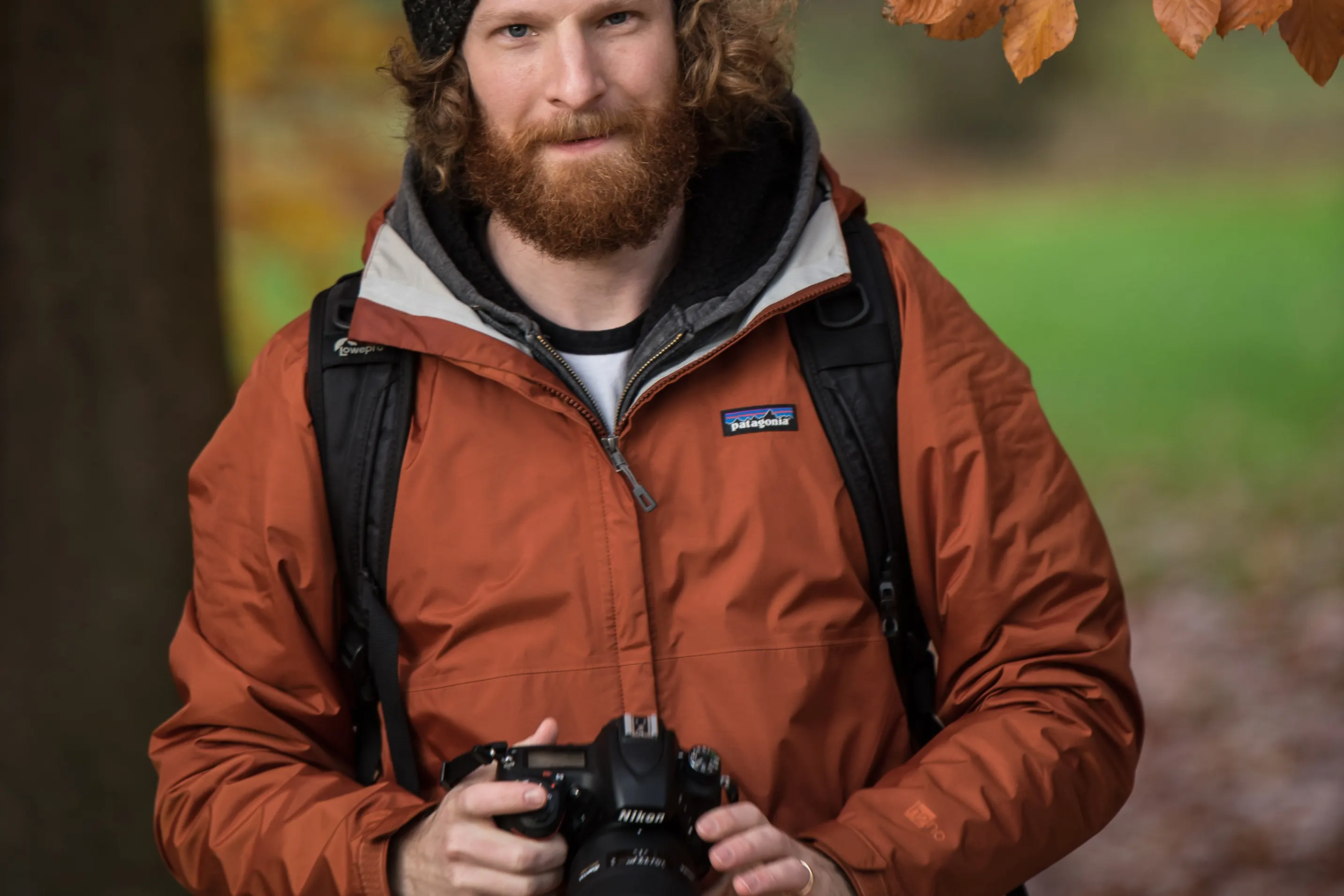 Man with a beard and a brown jacket holding a camera